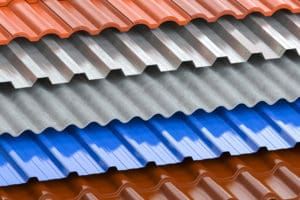 A close-up of stacked roofing sheets in various materials and colors, perfect for exterior renovations in Madison, WI. The layers include wavy red tiles on top and bottom, with corrugated metallic, silver, and blue sheets in between. The sheets contrast in texture and hue, showcasing different roofing options.