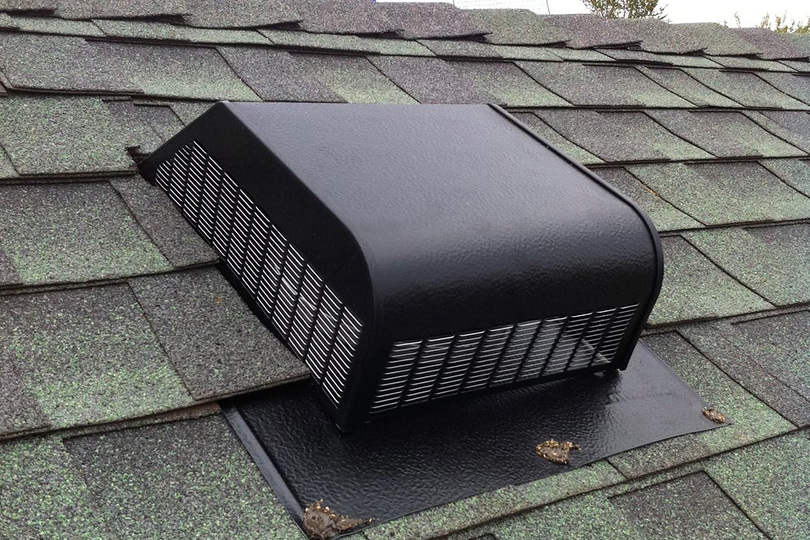 A black metal roof vent is installed on a roof with green asphalt shingles in Madison, WI. The vent has a curved, rectangular shape with side grilles for ventilation. As part of the exterior renovations, the shingles around the vent appear slightly weathered.