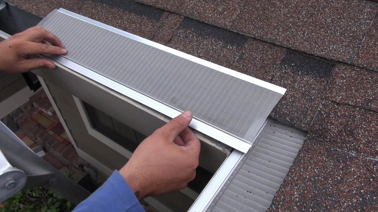 Close-up of a person installing a metal gutter guard on the edge of a shingled roof. The person is securing it by pressing into place, ensuring it fits correctly along the roofline. In the background, part of the house's exterior renovations is visible. This scene captures typical maintenance in Madison WI.