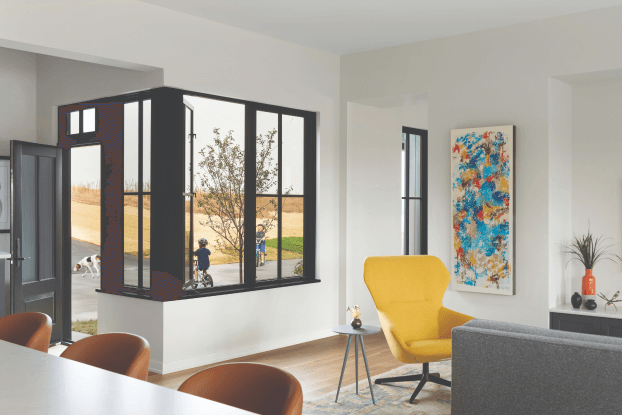 Modern living room with a large window showcasing recent exterior renovations, including a tree and bicycles outside. Inside, theres a gray sofa, a yellow armchair, and a small table with decor beneath a colorful abstract painting. Minimalist and bright setting.
