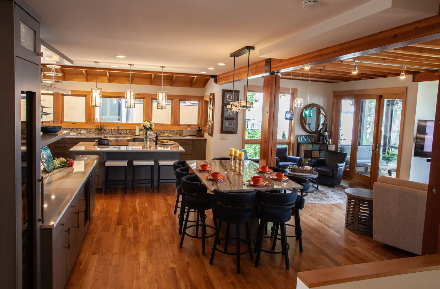 A spacious modern kitchen and living area featuring a large island with bar stools, pendant lighting, and wooden flooring. The space includes stainless steel appliances, a comfortable seating area, and large windows and doors that let in ample natural light—perfect for homes in Madison WI considering exterior renovations.